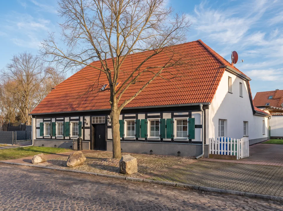 Der Alte Krug in Ludwigsfelde, ein langes Fachwerkhaus mit grünen Fensterläden und rotem Ziegeldach in der Sonne