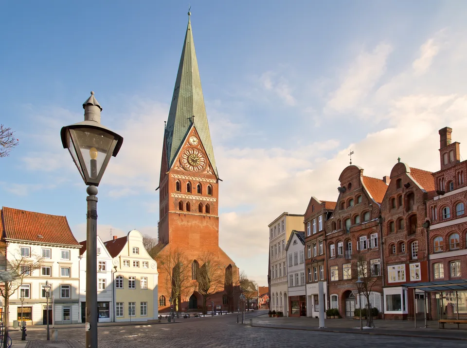 Der Platz Am Sande in Lüneburg mit Backstein-Giebelhäusern und dem hohen Turm der Kirche St. Johannis mit grüner Spitze
