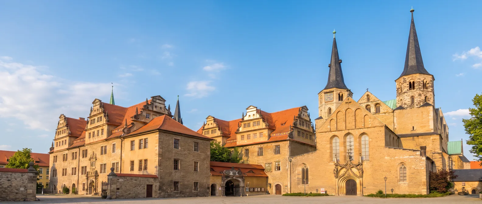 Der Merseburger Dom mit seinen zwei spitzen Westtürmen und das Renaissance-Schloss Merseburg mit roten Dächern am Domplatz bei Sonnenschein