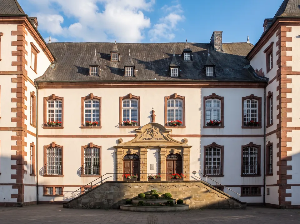 Das historische Stadthaus von Merzig mit weißer Fassade, roten Sandsteinrahmen, Ecktürmen und Freitreppe