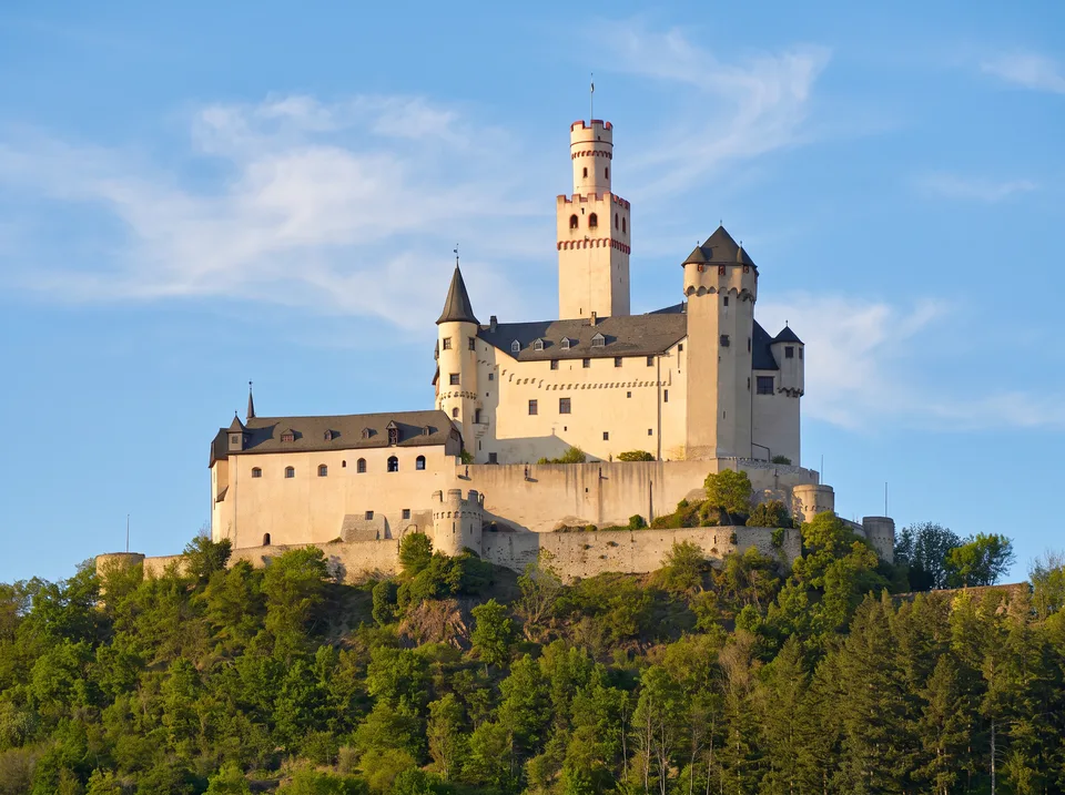 Marksburg mit hohem Bergfried und hellen Mauern auf einem bewaldeten Felskegel über Braubach