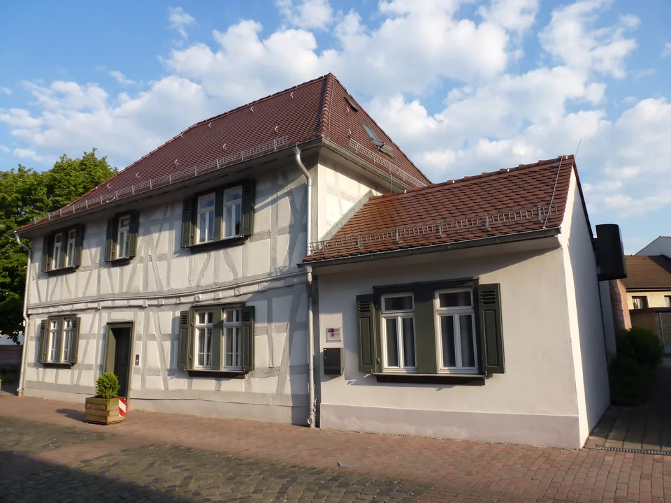 Die Französische Schule in der Pfarrgasse in Neu-Isenburg, ein weißes Fachwerkhaus mit grünen Fensterläden und rotem Ziegeldach