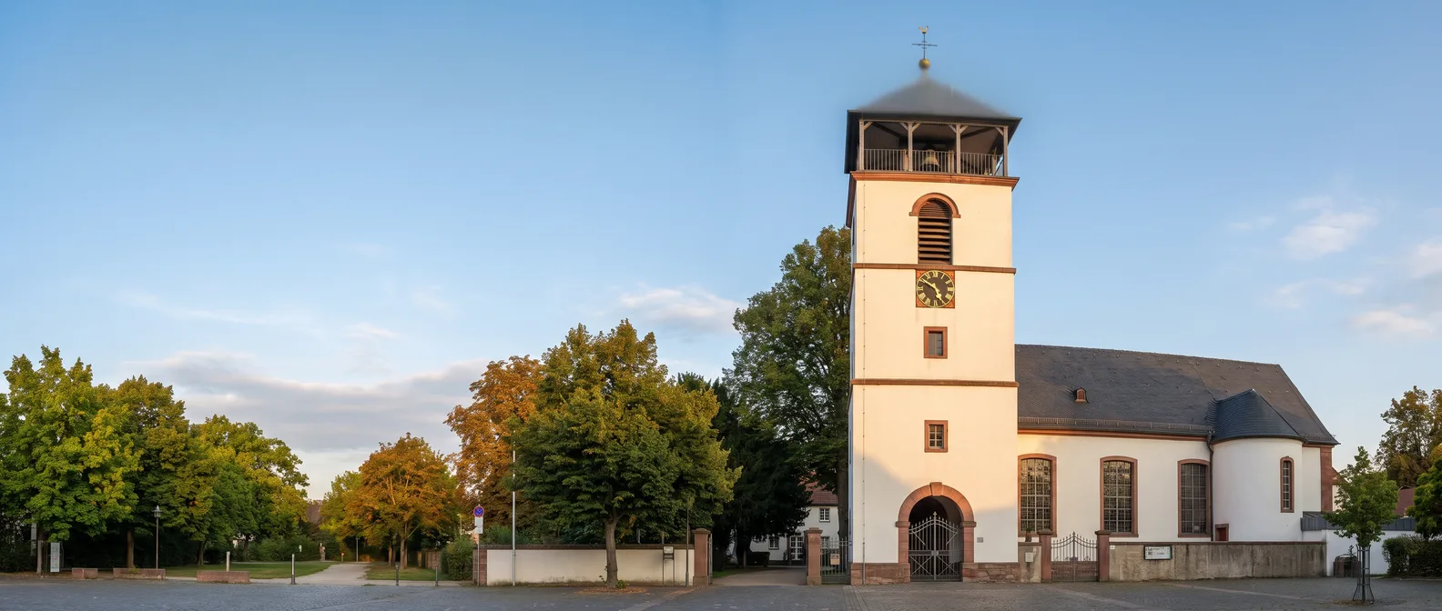 Die evangelisch-reformierte Kirche in Neu-Isenburg mit weißem Turm, Uhr und offener Glockenstube im warmen Abendlicht
