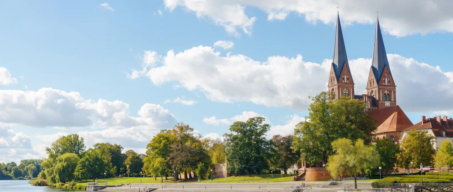 Die Klosterkirche St. Trinitatis in Neuruppin mit ihren zwei spitzen Backsteintürmen über den Bäumen am Ufer des Ruppiner Sees
