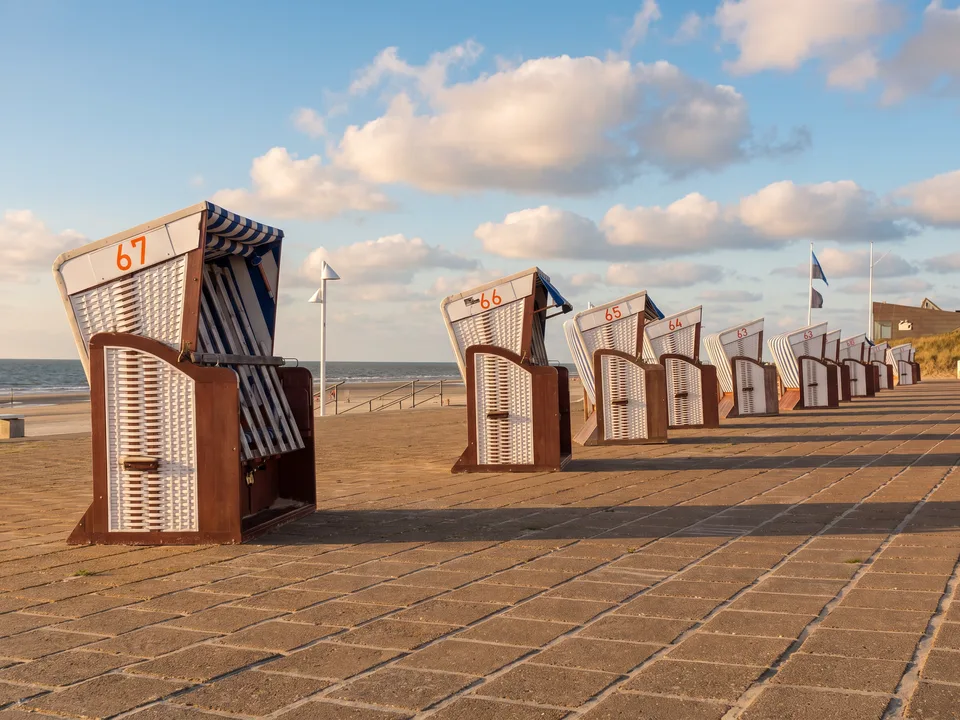 Reihe weiß-blau gestreifter Strandkörbe auf der Strandpromenade von Norderney, links die Nordsee