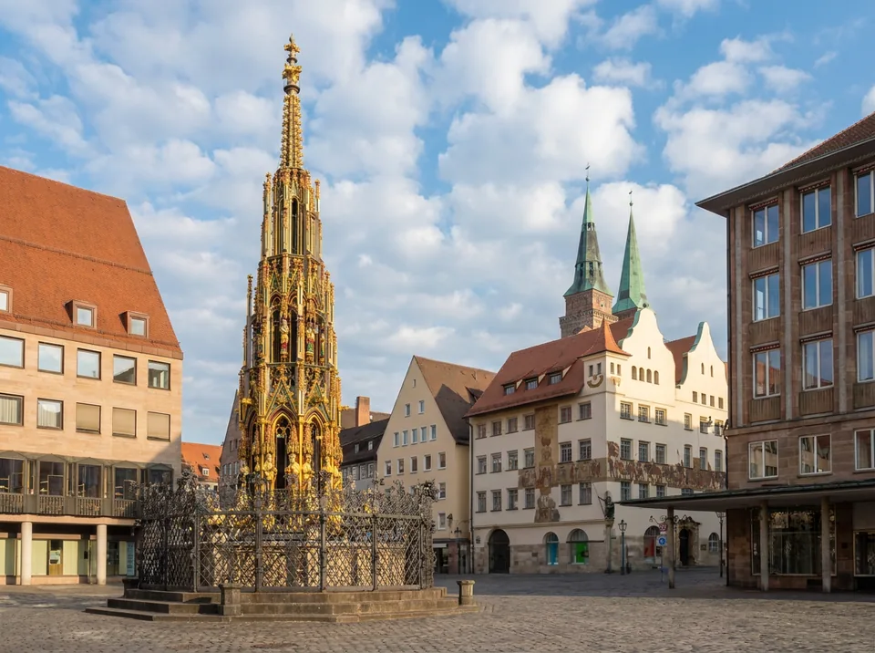 Schöner Brunnen auf dem Nürnberger Hauptmarkt mit vergoldeter gotischer Turmspitze und Kirchtürmen von St. Sebald