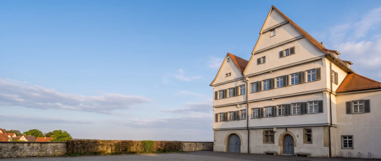 Die weiße Propstei im Klosterhof von Nellingen in Ostfildern mit zwei steilen Giebeln, roten Ziegeldächern, Fensterläden und zwei Rundbogenportalen im Abendlicht