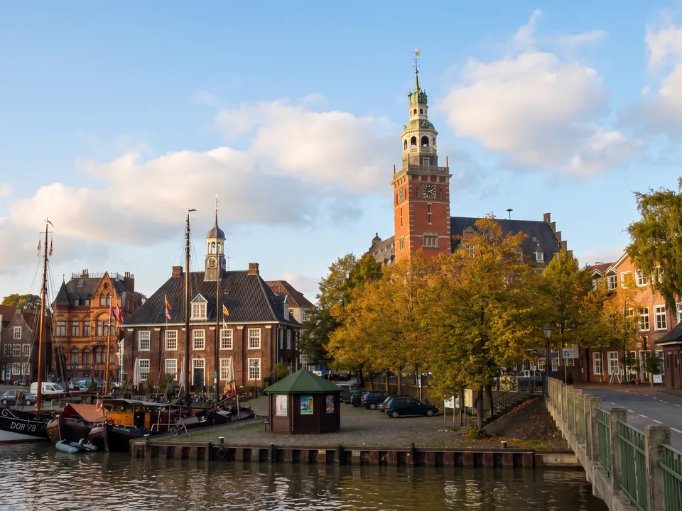 Historisches Rathaus von Leer mit hohem Turm und die Waage am Hafen mit Traditionsschiffen im Herbstlicht