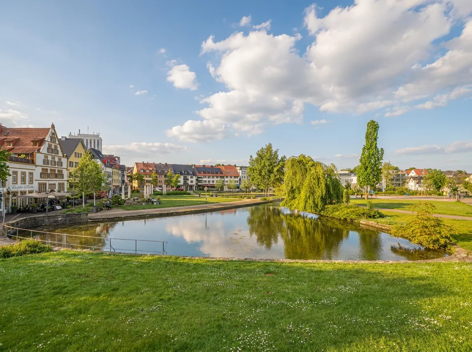 Klares Quellbecken der Pader mit Wiesen, Trauerweide und Altstadthäusern in Paderborn