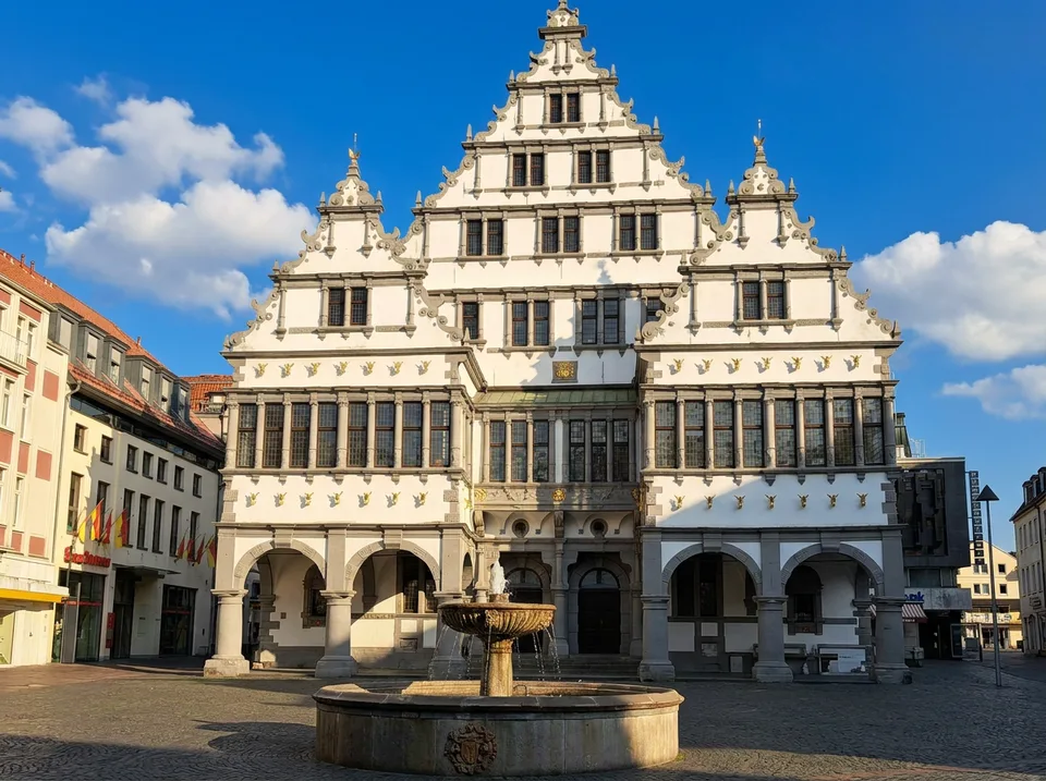 Weißes historisches Rathaus in Paderborn mit drei Renaissance-Giebeln, Arkaden und Brunnen davor