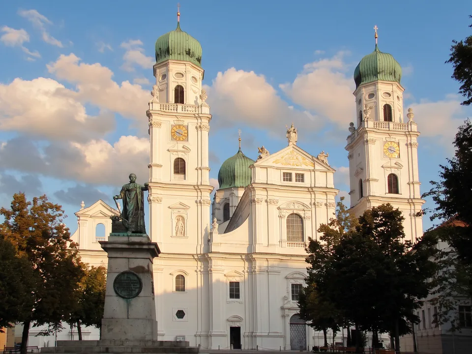 Die weiße Westfassade des Doms St. Stephan in Passau mit zwei grünen Zwiebeltürmen und dem Denkmal von König Max I. Joseph