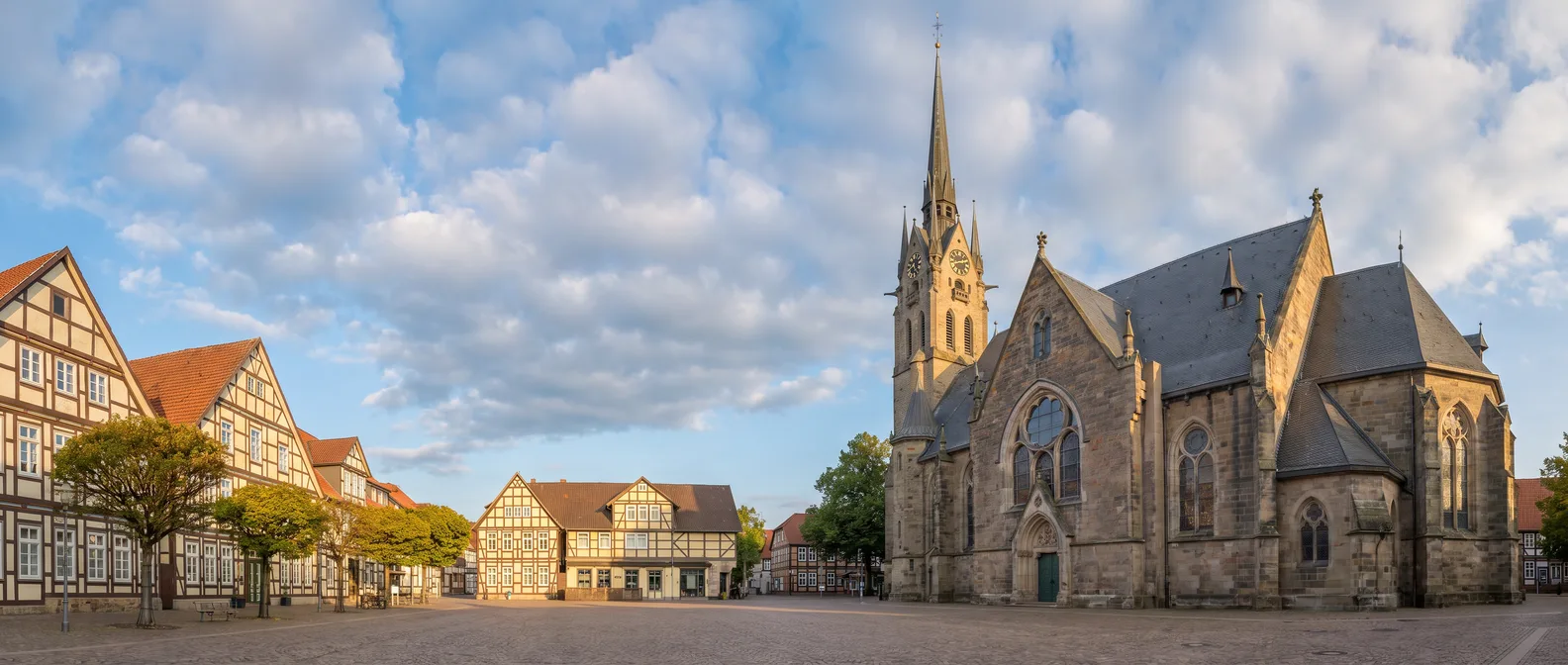 Neugotische St.-Jakobi-Kirche aus Sandstein mit hohem Turm, vier Uhrgiebeln und schlanker Spitze, daneben Fachwerkhäuser auf einem gepflasterten Platz im goldenen Abendlicht