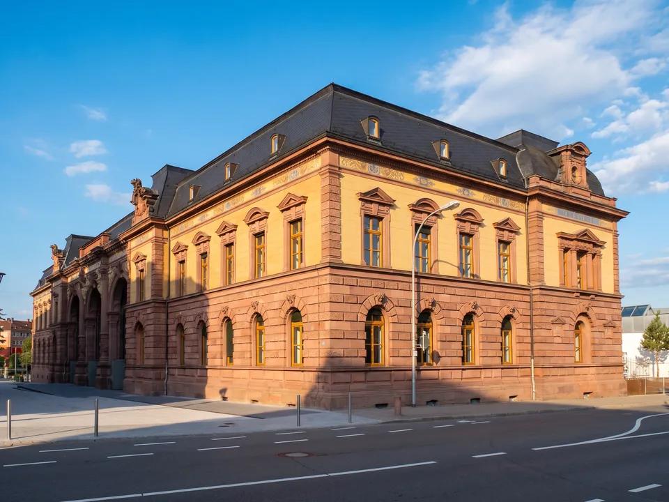 Die Alte Post in Pirmasens, ein prachtvoller Neorenaissance-Bau aus rotem Sandstein mit gelber Fassade und dunklem Schieferdach, im Sonnenlicht