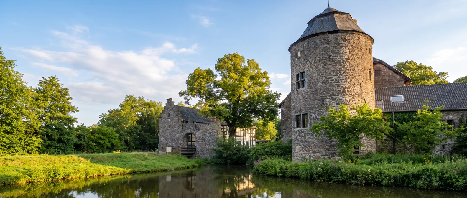 Wasserburg Haus zum Haus in Ratingen mit rundem Bruchsteinturm und Burggraben im warmen Spätsommerlicht