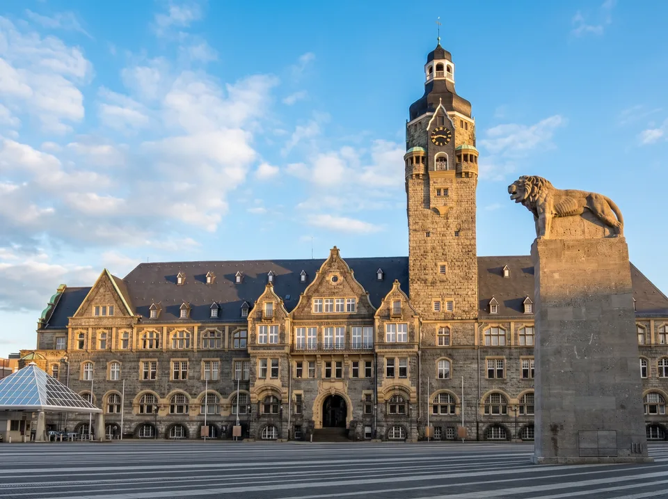 Das Remscheider Rathaus aus grauem Naturstein mit hohem Rathausturm und Löwendenkmal im Sonnenlicht