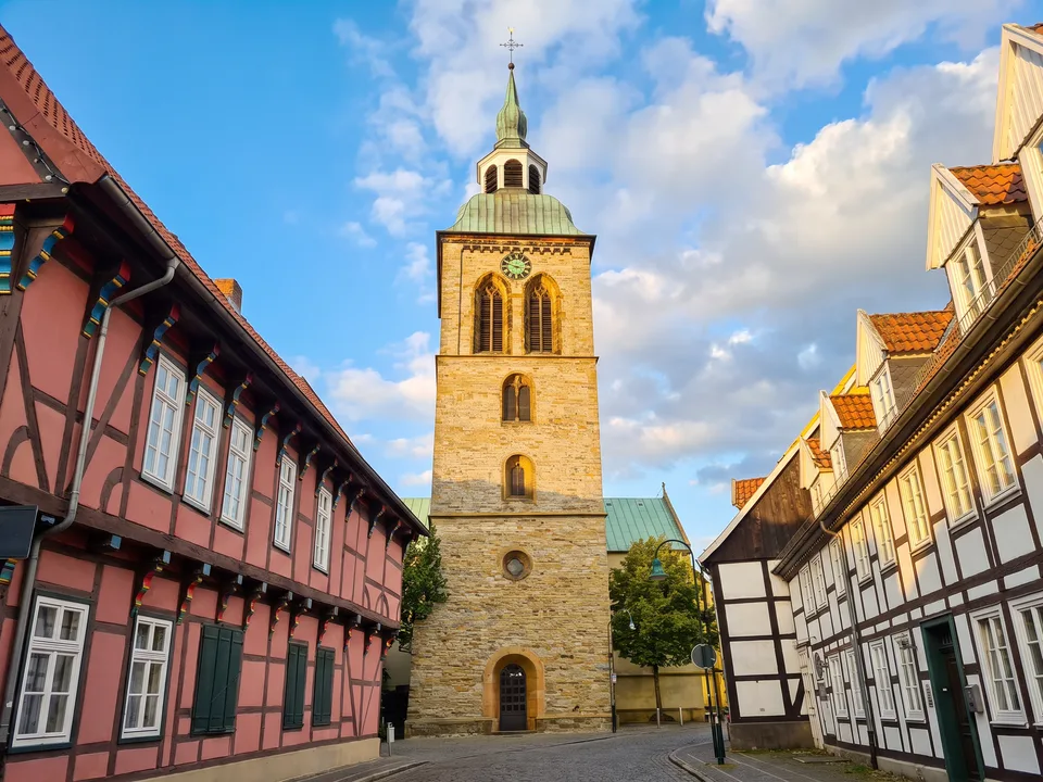Der Sandsteinturm der Kirche St. Aegidius in Wiedenbrück mit grüner Haube zwischen Fachwerkhäusern