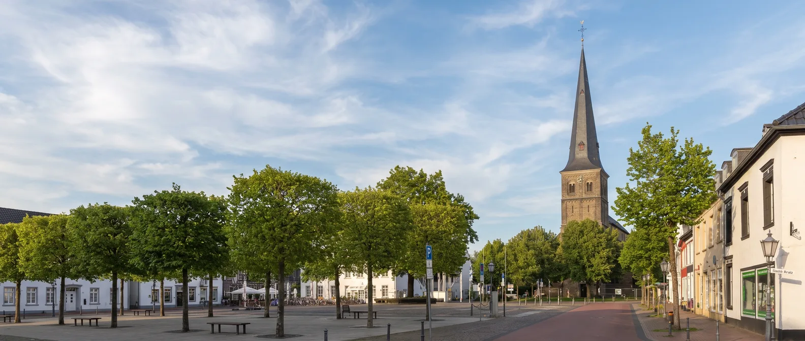Der Turm der Pfarrkirche St. Peter mit spitzem Schieferhelm über den Bäumen am Marktplatz von Rheinberg