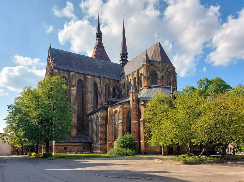 Die backsteingotische Marienkirche in Rostock mit spitzen Türmen und Bäumen im Sonnenlicht
