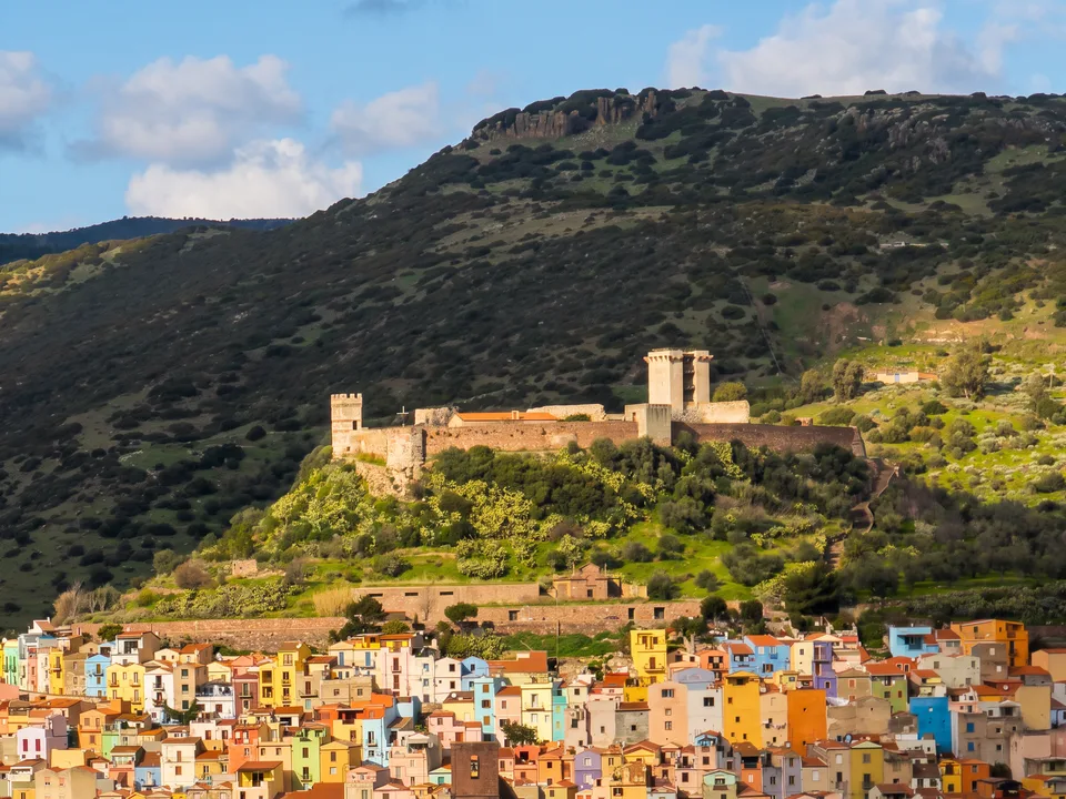 Die bunten Häuser der Altstadt von Bosa unterhalb der Burg Malaspina auf dem grünen Hügel