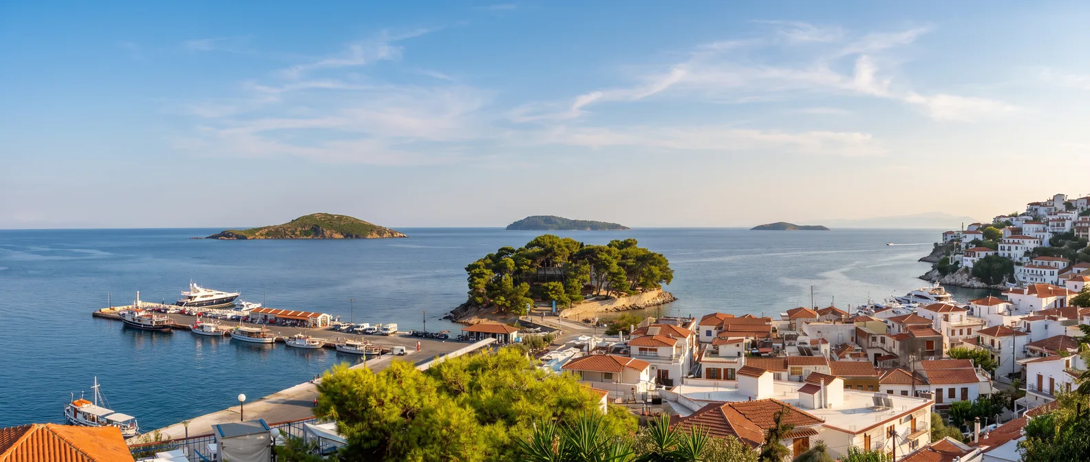 Blick über die rot gedeckten Häuser von Skiathos-Stadt auf die kiefernbewachsene Halbinsel Bourtzi, den Hafen und kleine Inseln in der Ägäis
