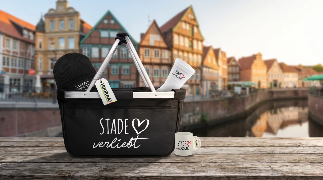 Schwarzer Einkaufskorb „Stade verliebt“ mit Beanie und Socken, daneben die Kaffeetasse, auf einem Holztisch am Hansehafen
