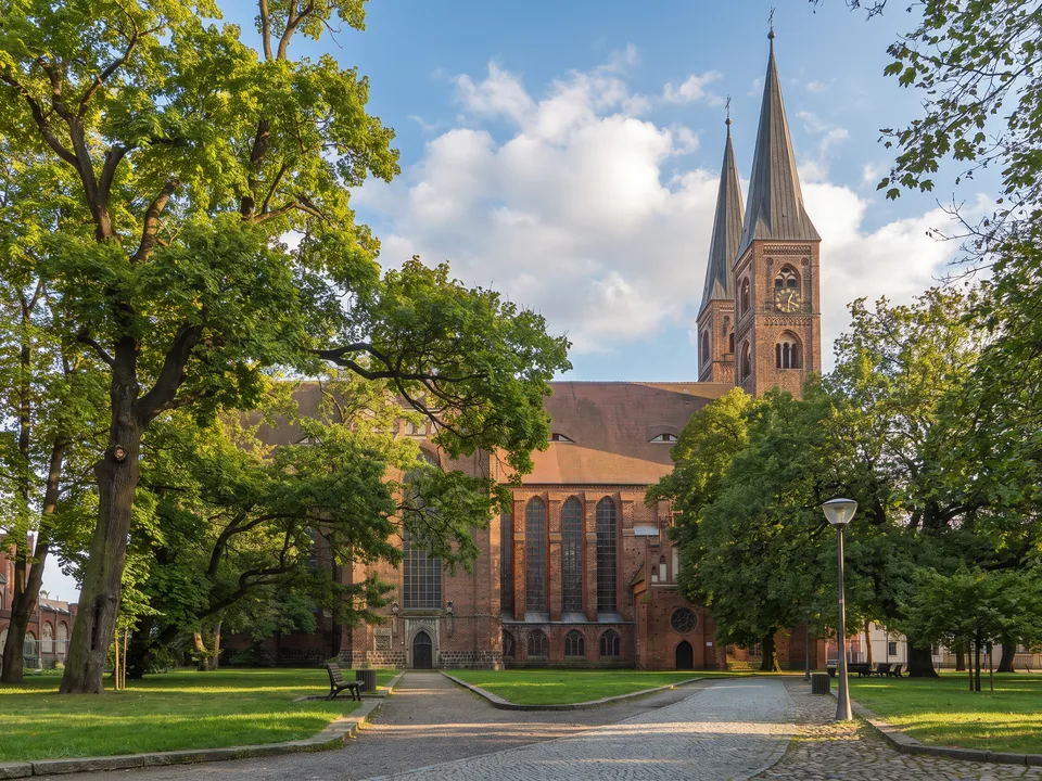 Der Dom St. Nikolaus in Stendal mit zwei spitzen Westtürmen hinter alten Bäumen und einer Wiese