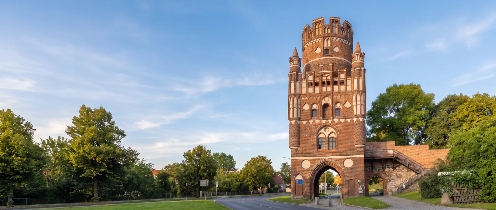 Das Uenglinger Tor in Stendal, ein hoher Backsteinturm mit weißen Blenden, Ecktürmchen und Zinnenkranz, unter blauem Himmel