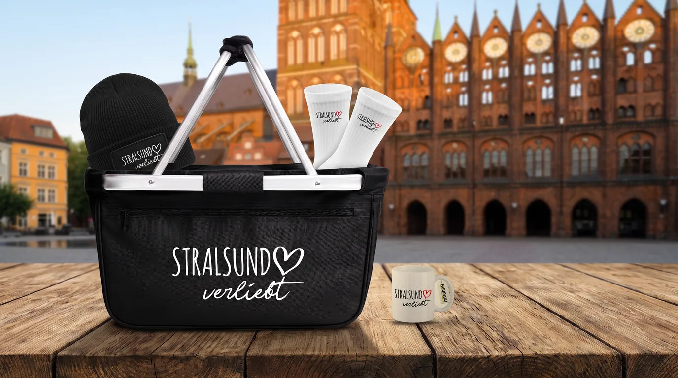 Faltbarer Einkaufskorb Stralsund verliebt mit Beanie und Socken, daneben eine Kaffeetasse, auf einem Holztisch vor dem Stralsunder Rathaus