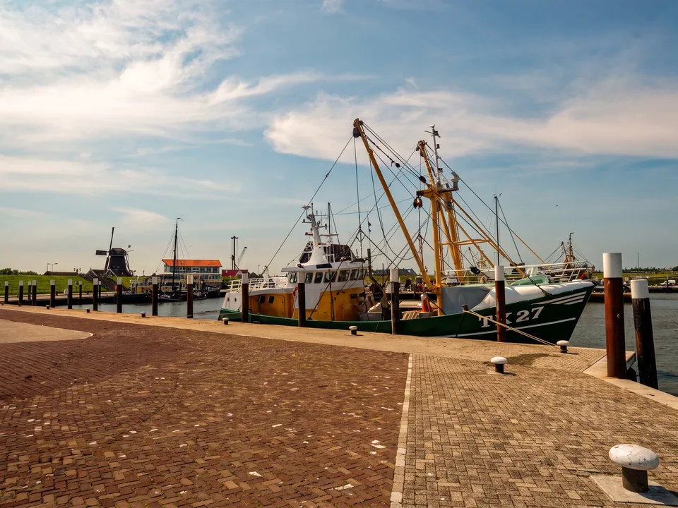 Fischkutter am gepflasterten Kai im Hafen von Oudeschild, im Hintergrund eine Windmühle und Hafengebäude