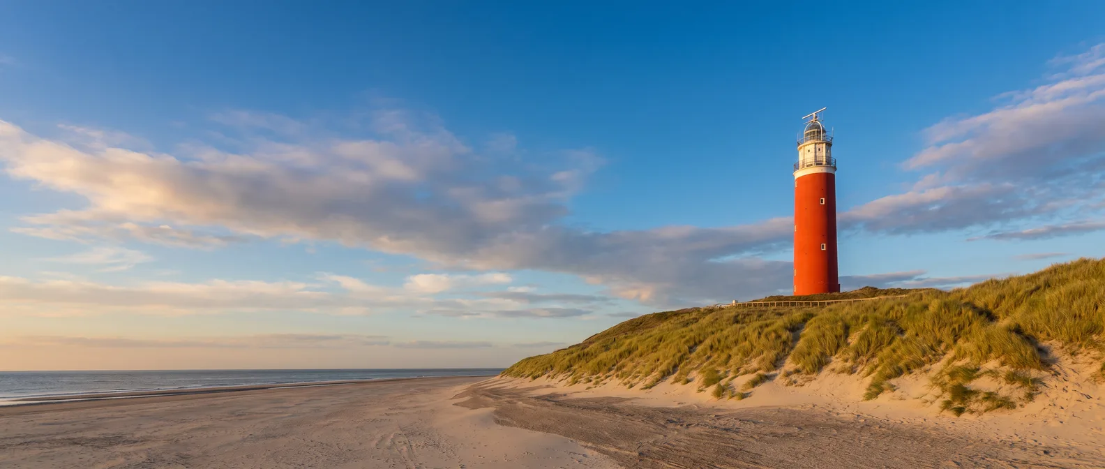 Roter Leuchtturm Eierland auf der grasbewachsenen Düne über dem breiten Nordseestrand von Texel im goldenen Abendlicht