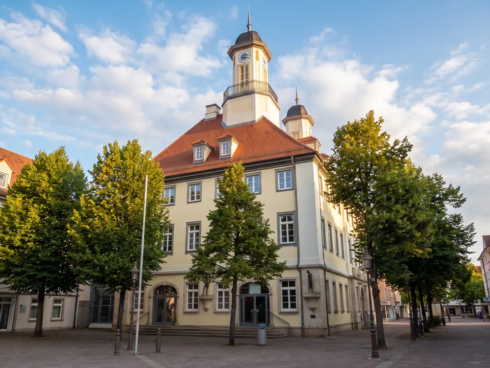 Das helle Rathaus von Tuttlingen mit rotem Walmdach, zwei Türmen und Bäumen davor unter blauem Himmel