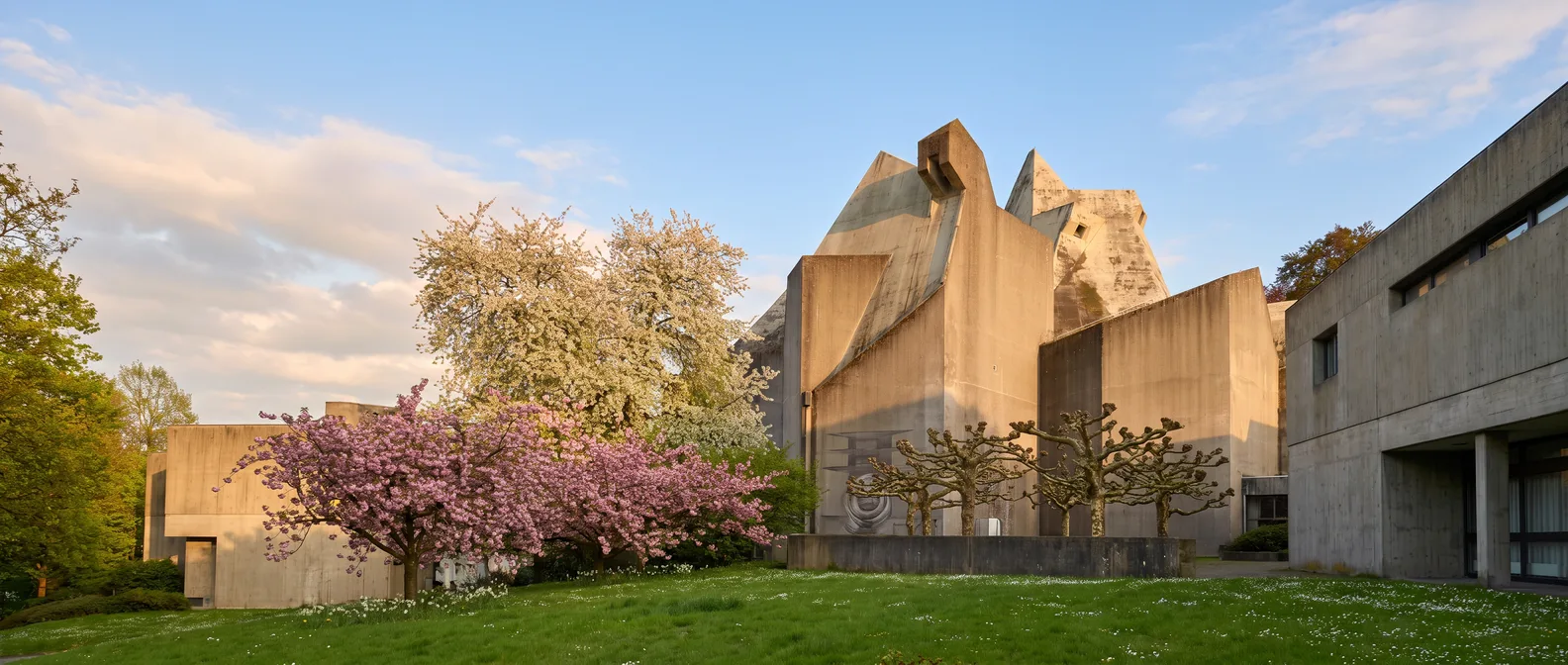 Der Mariendom in Velbert-Neviges mit seinen gefalteten Betondächern hinter einer grünen Wiese und blühenden Bäumen