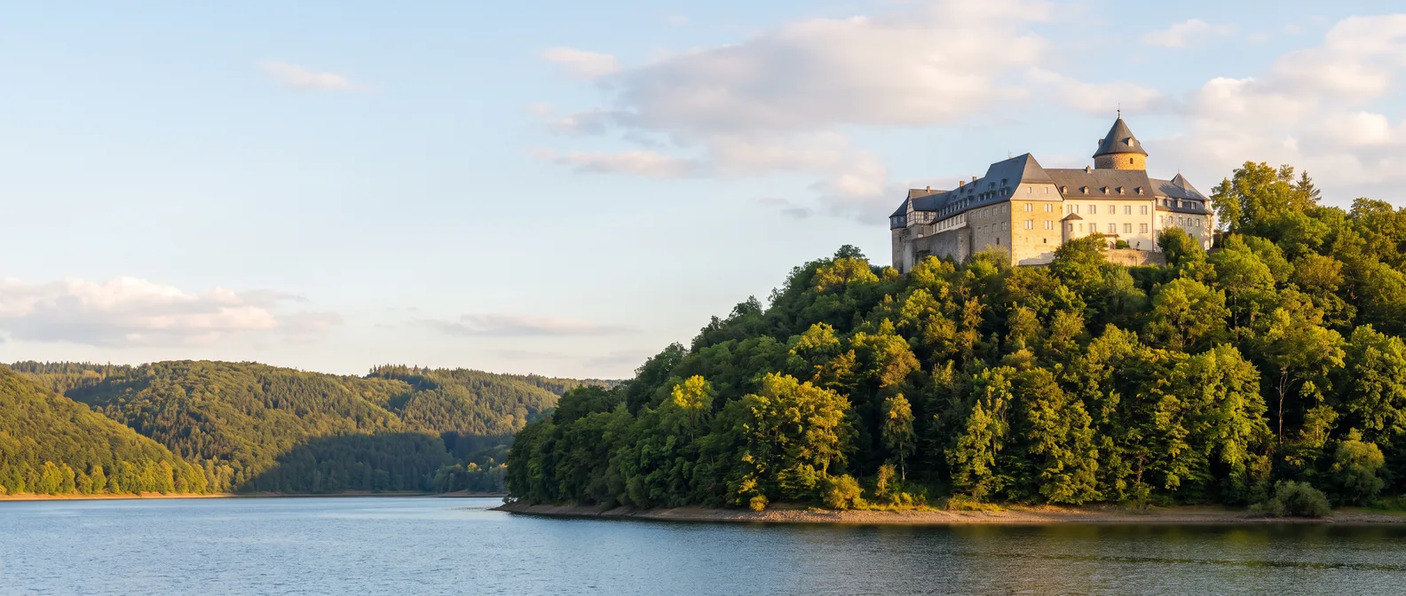 Schloss Waldeck auf einem bewaldeten Berg über dem Edersee im Abendlicht