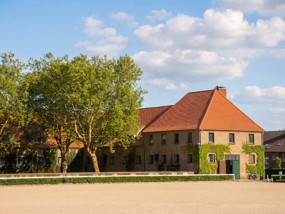Stallgebäude aus gelbem Backstein mit roten Ziegeldächern und Reitplatz im Landgestüt Warendorf