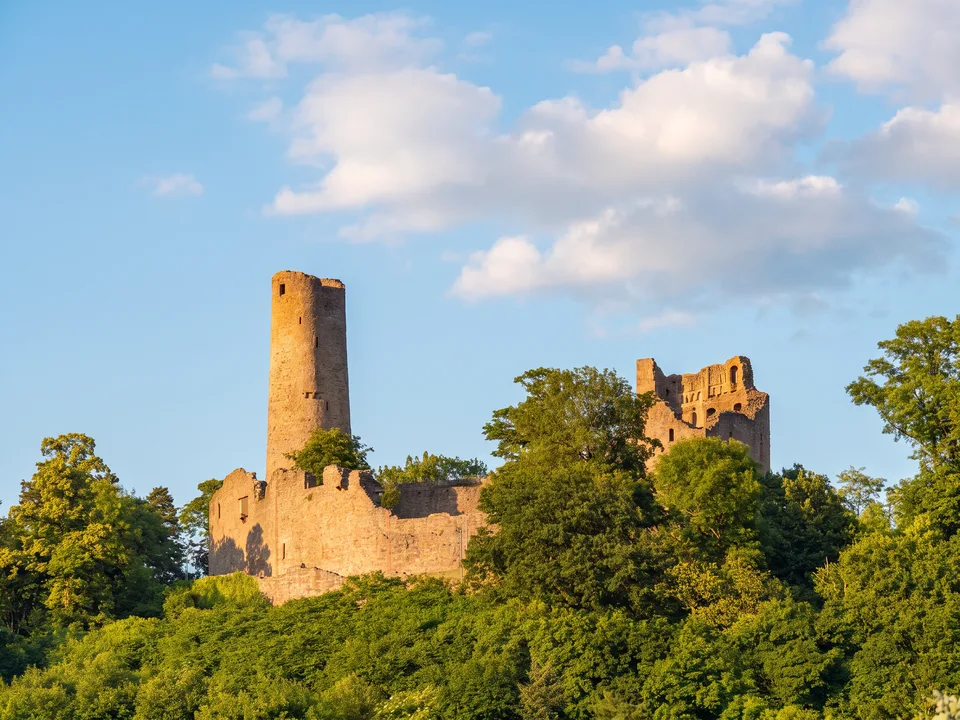 Die Burgruine Windeck mit rundem Bergfried und Mauerresten über grünen Bäumen