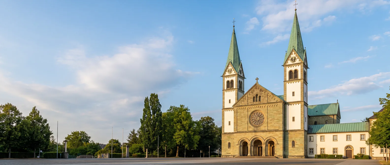 Die Wallfahrtsbasilika Mariä Heimsuchung in Werl aus Sandstein mit zwei grünen Turmspitzen und Rosettenfenster unter blauem Himmel