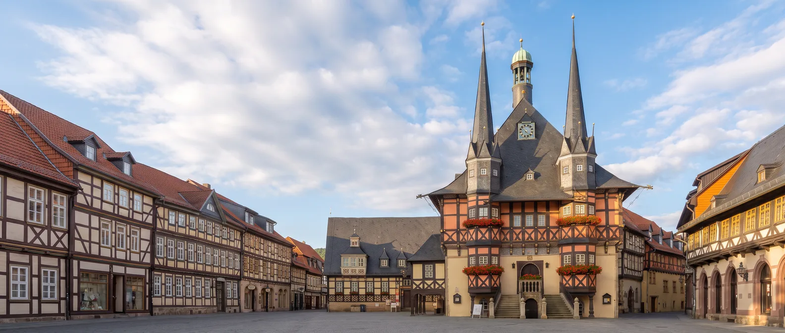 Das Fachwerk-Rathaus von Wernigerode mit zwei spitzen Schiefertürmen, Blumenkästen und Freitreppe am Marktplatz unter blauem Himmel