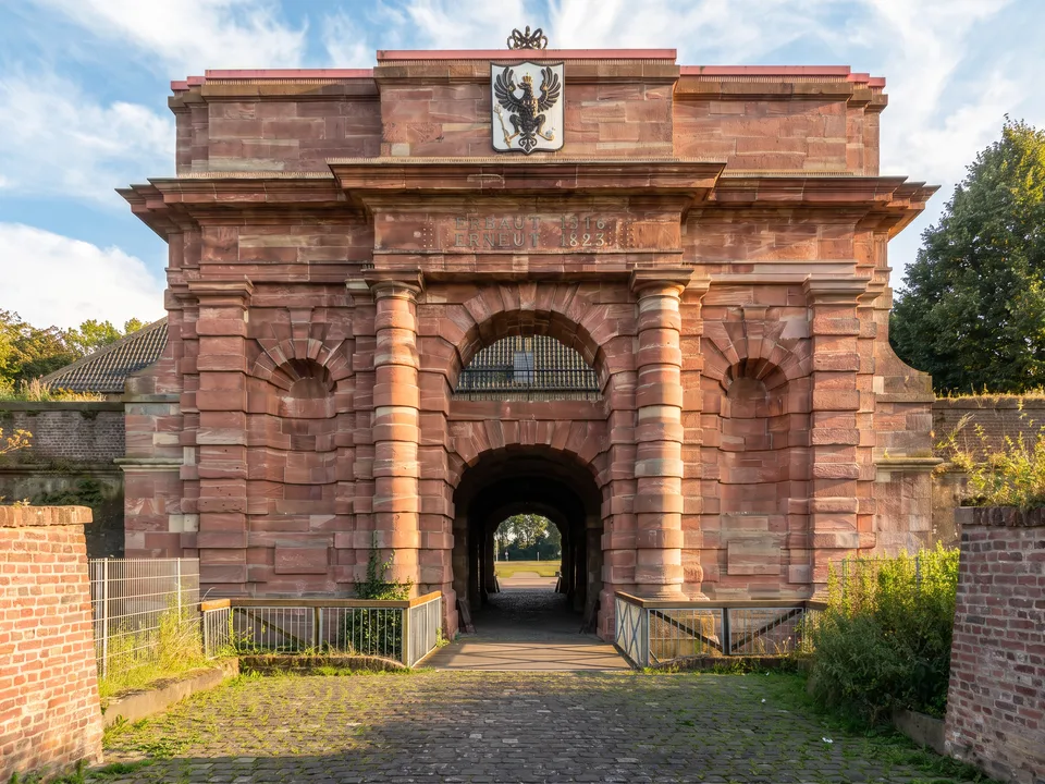 Haupttor der Zitadelle Wesel aus rotem Sandstein mit Adlerwappen, davor eine Holzbrücke, unter blauem Himmel