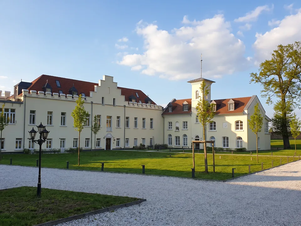 Die Godorfer Burg in Wesseling-Berzdorf mit hellem Hauptbau, Treppengiebel und schlankem Turm hinter einer Rasenfläche