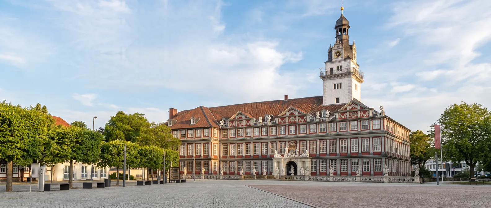 Schloss Wolfenbüttel mit rot-weißer Barockfassade, Figurenportal und hohem weißem Schlossturm am weiten Schlossplatz unter blauem Himmel